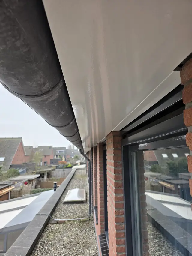 Wit gelakt dakgoot- en boeiwerk onder een dakoverstek