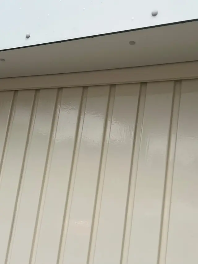Crèmekleurige houten gevelbekleding onder een dakoverstek