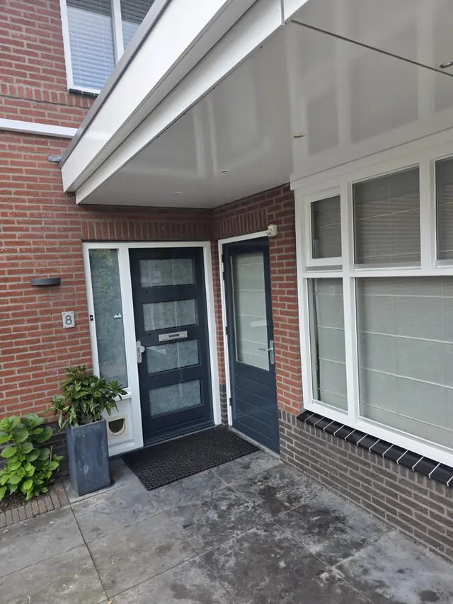 Geschilderde antracietkleurige voordeur met wit gelakt kozijnwerk onder een luifel