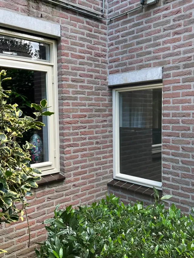 Twee wit gelakte kozijnen op de hoek van een woning, in twee lagen aflak met nieuwe beglazingskit